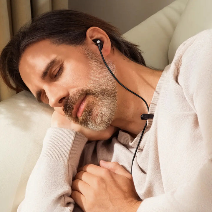 man resting with ear-worn vagus nerve wellness device